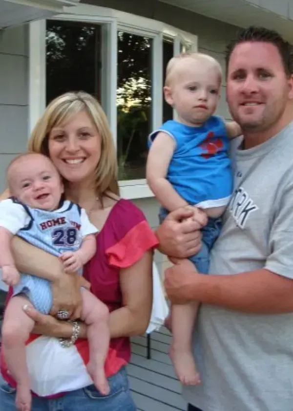 Family of four posing outdoors; mother and father holding toddlers.