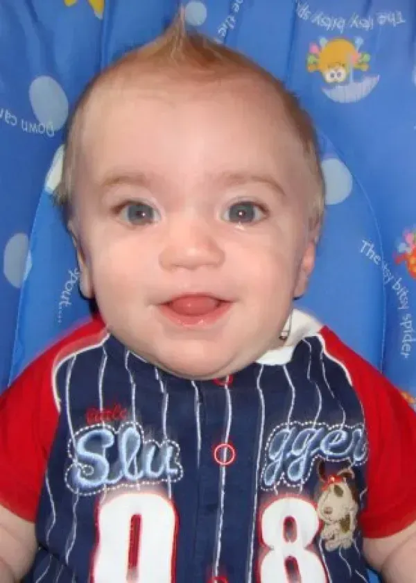 Smiling baby with a spiky mohawk hairstyle wearing a baseball jersey.