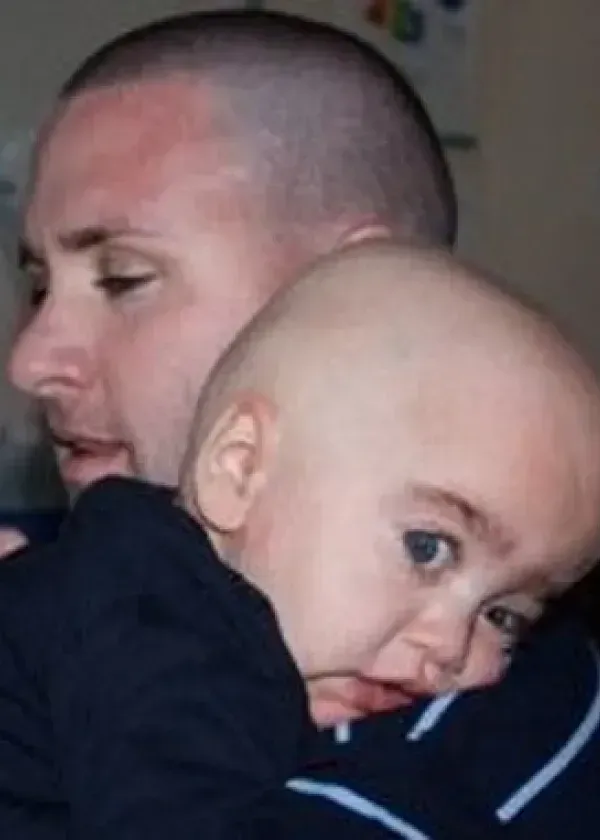 Man holding a bald baby, both looking off-camera.