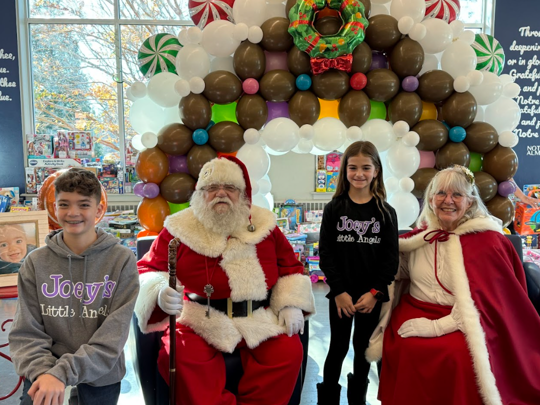 Two children with Santa and Mrs. Claus under a gingerbread arch. Festive setting with balloons.
