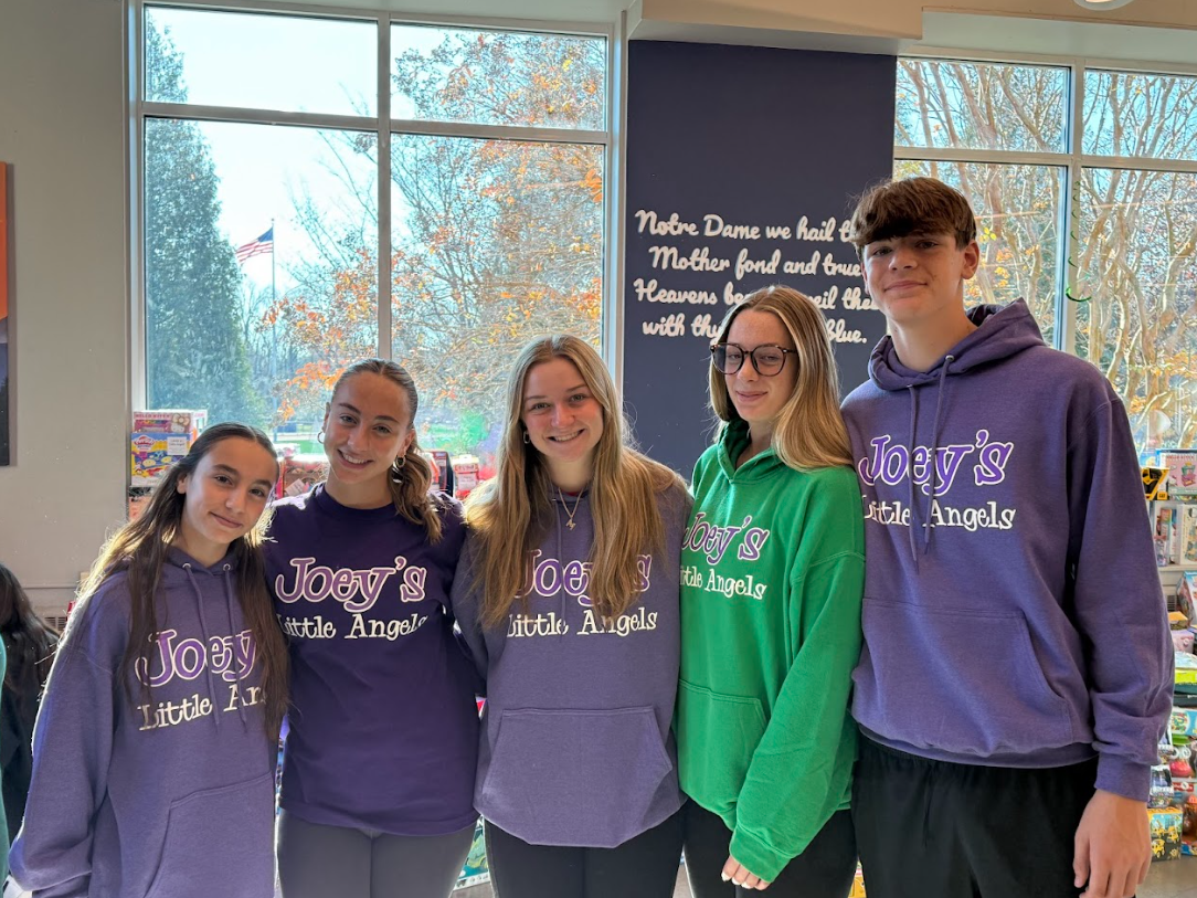 Five people wearing sweatshirts with a logo in front of a window. Some are smiling.