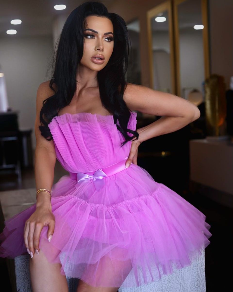 A woman in a pink tulle dress is sitting on a stool.