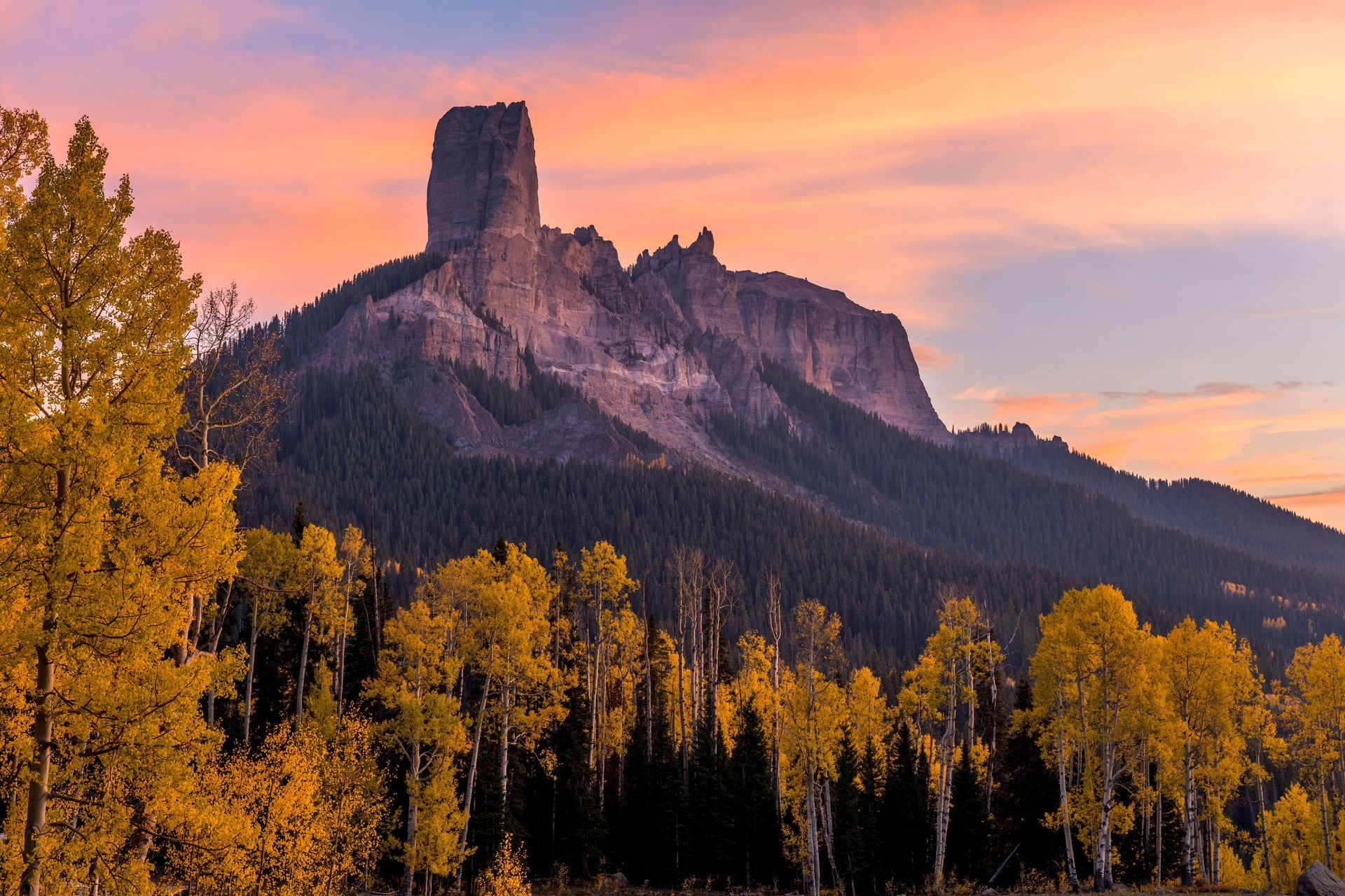 a mountain with a sunset in the background and trees in the foreground .