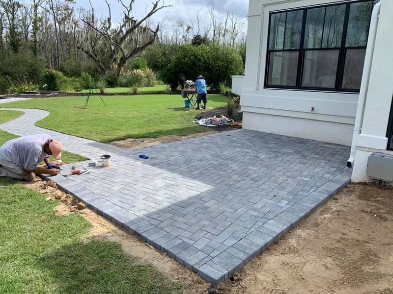 Workers installing gray brick patio next to a house with a brick walkway in the yard.
