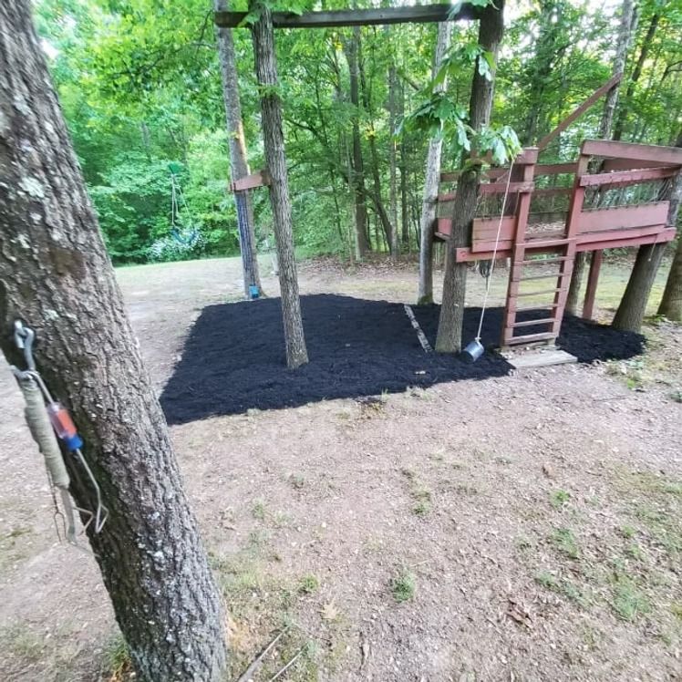 Wooded playground with a wooden climbing platform and fresh black mulch beneath the play area.
