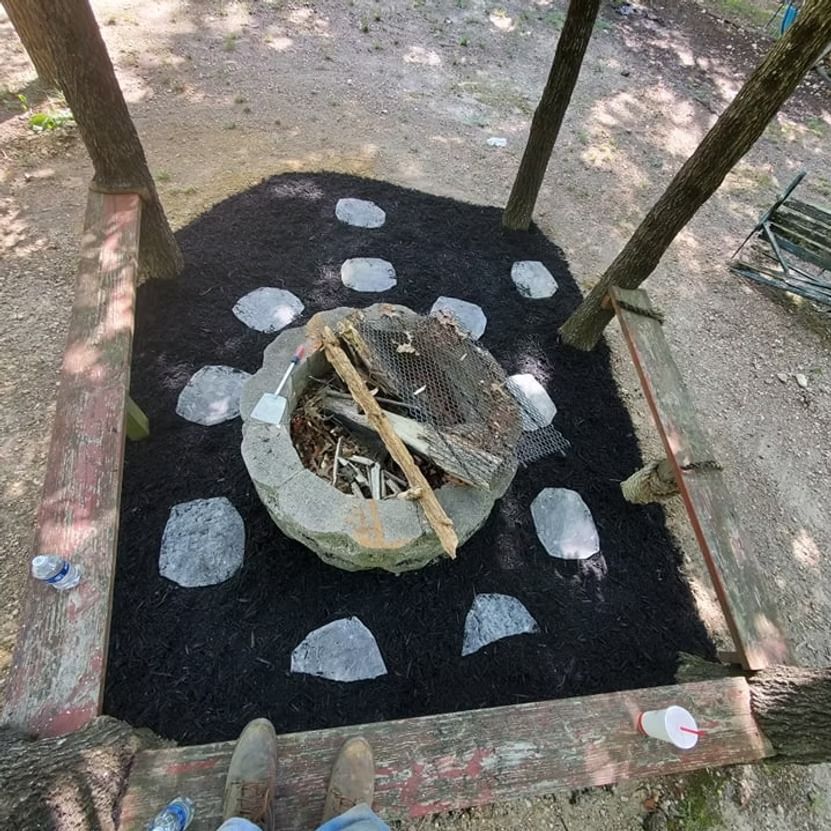 Outdoor fire pit surrounded by white painted stones on black ground, framed by a wooden structure