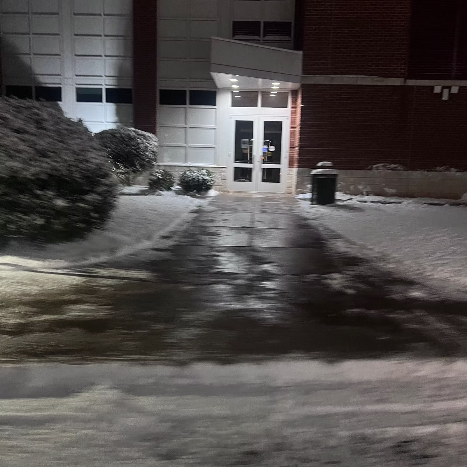 Snowy building entrance at night with lit double doors and wet pavement