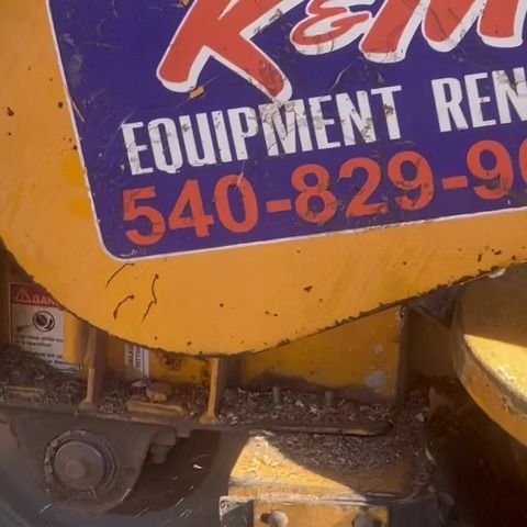 Close-up of a yellow rental machine with a purple K&M Equipment Rentals sign and phone number.