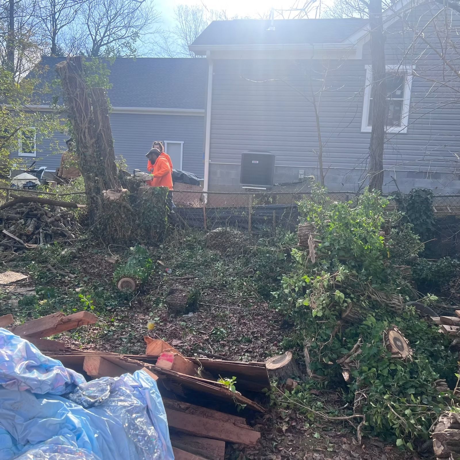 Person in orange jacket amid storm debris in a yard beside a house