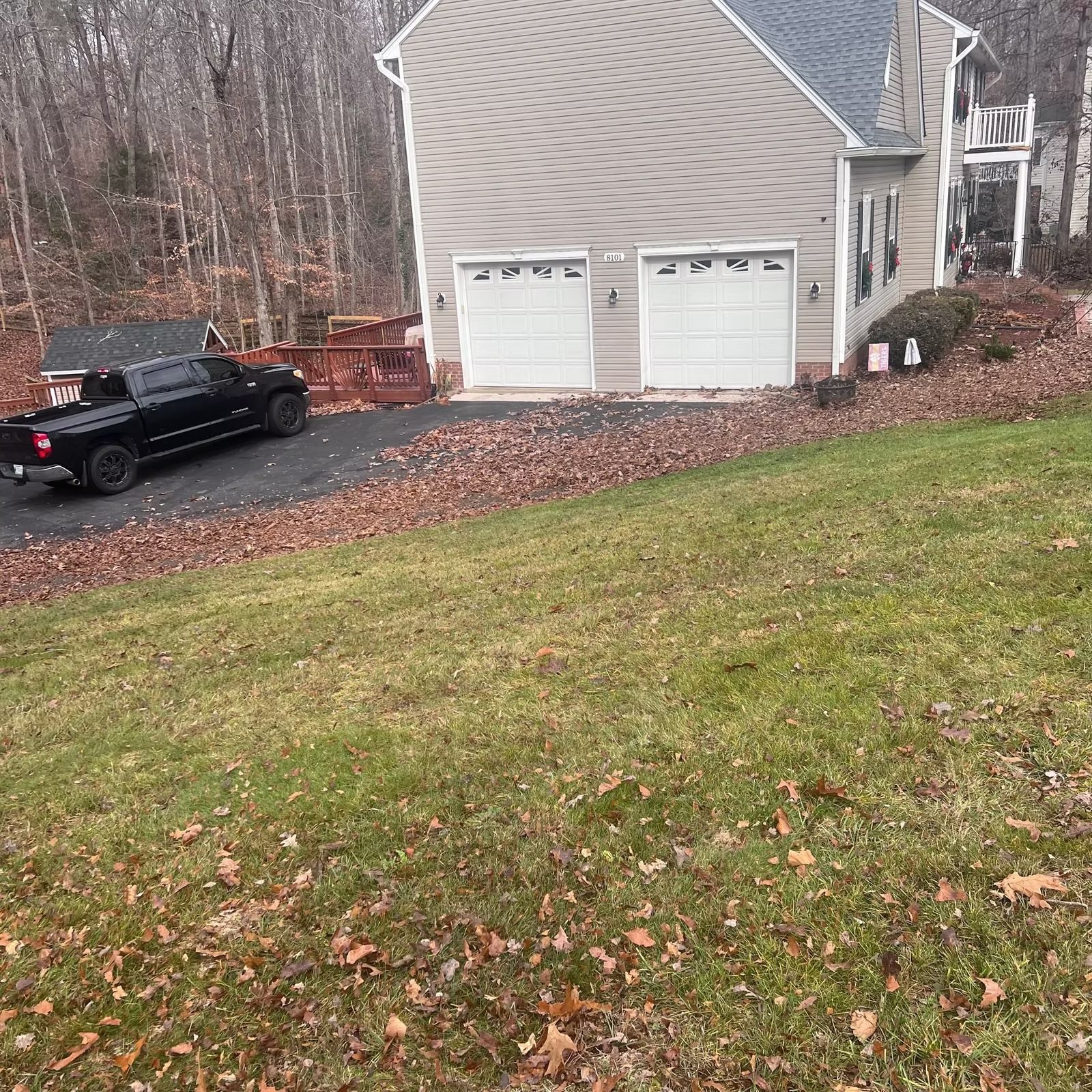 Black pickup truck parked on a driveway beside a two-car garage and a grassy yard in late fall.