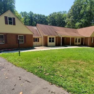 Suburban house with brick and tan siding, red roof, and a large green lawn under a sunny sky