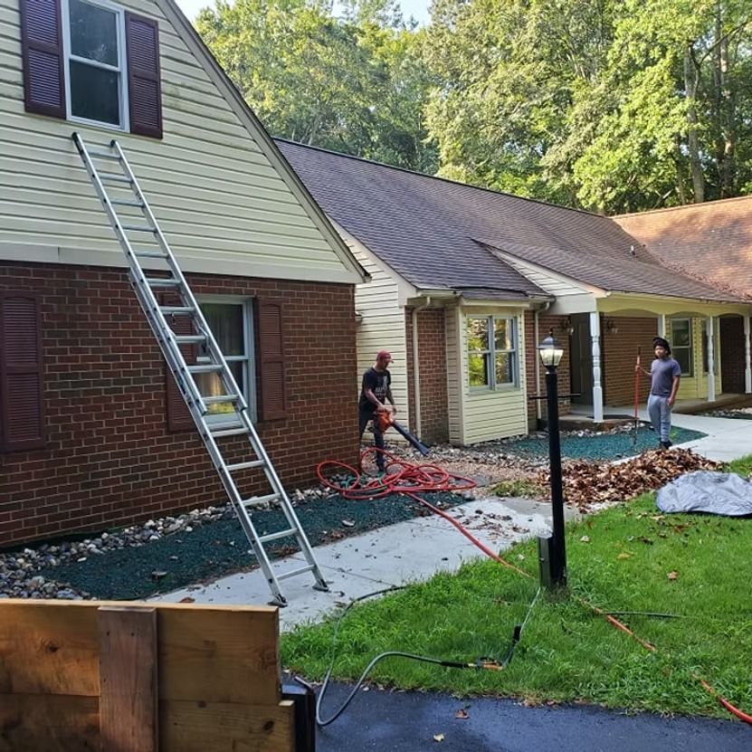 Workers on a roof and by the house during exterior renovation, with ladders and tools in the yard.