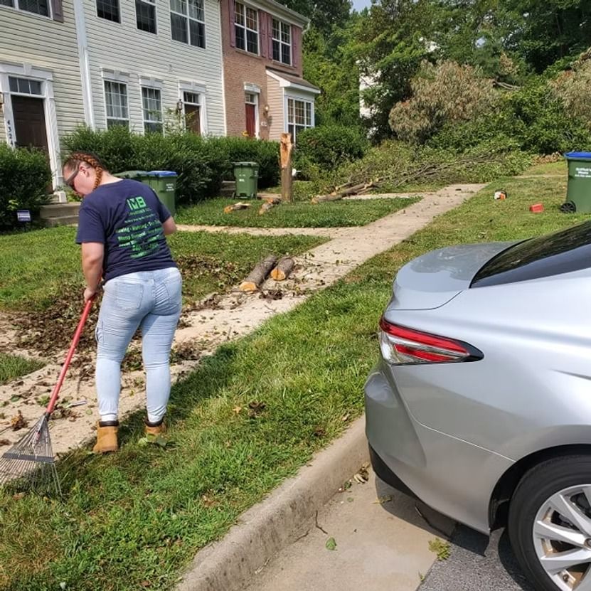Person raking dirt beside a townhouse sidewalk, with a silver car parked in the foreground.