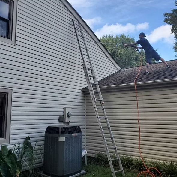 Worker on a roof using a hose near a ladder beside a house and air conditioner unit