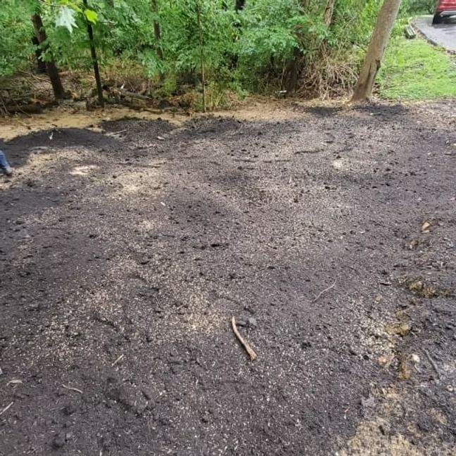 Freshly spread dark soil in a garden area beside trees and a grassy path