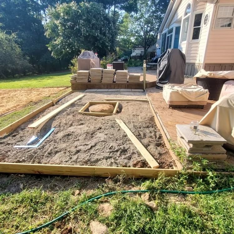 Backyard patio construction with a framed gravel bed and stacked pavers beside a house