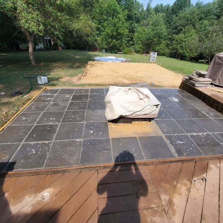 Backyard patio with dark tile, covered grill, and a tarp-covered area leading to a grassy yard and trees