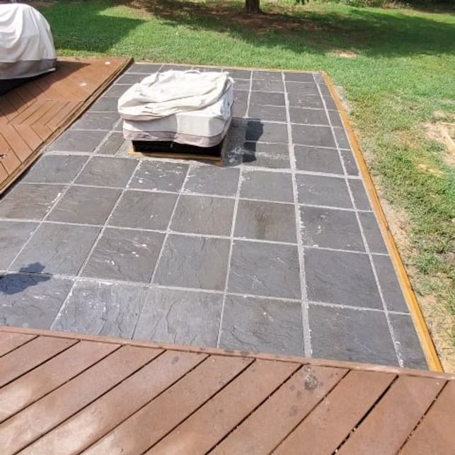 Patio with dark gray stone tiles bordered by wooden decking and a covered outdoor chair.