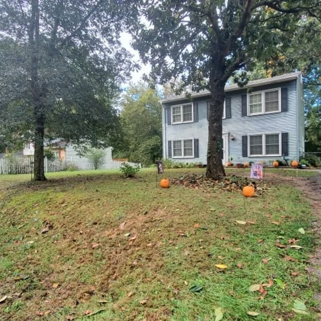 Suburban house with gray siding and autumn yard, with pumpkins near the front porch and trees in the lawn