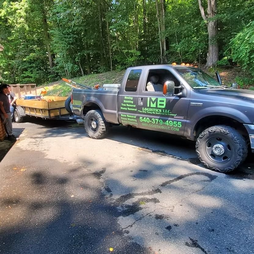 Dark gray pickup truck towing a trailer on a wooded dirt road, with a driver visible in the cab.