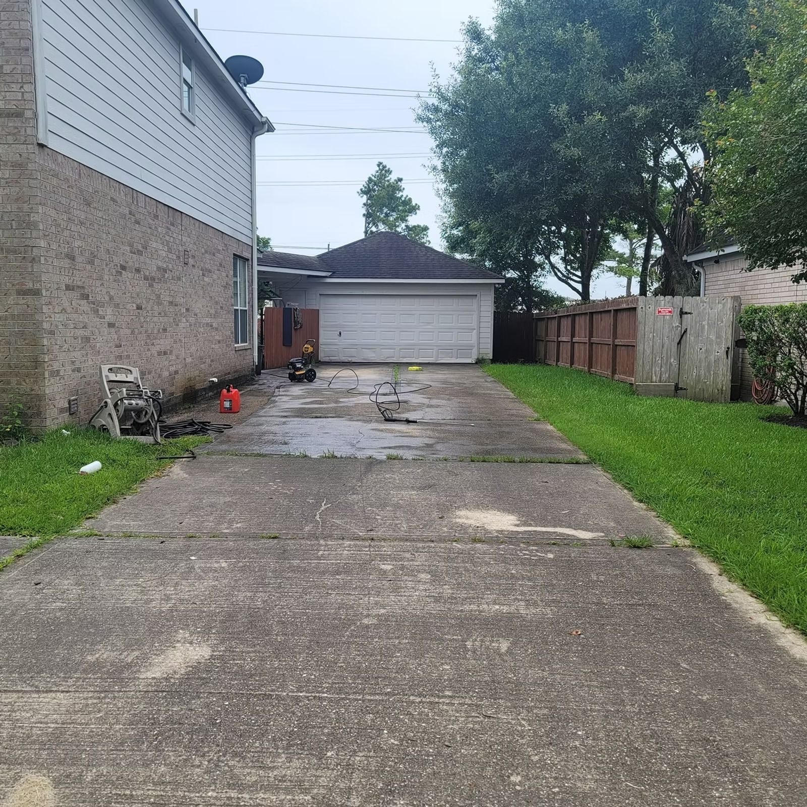 Concrete driveway leading to a detached garage beside a house, with grass and a wooden fence.