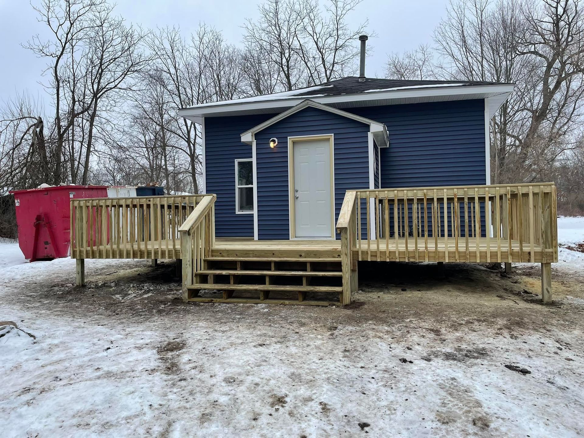 Blue building with wooden deck in a snowy setting. A red dumpster is on the left.