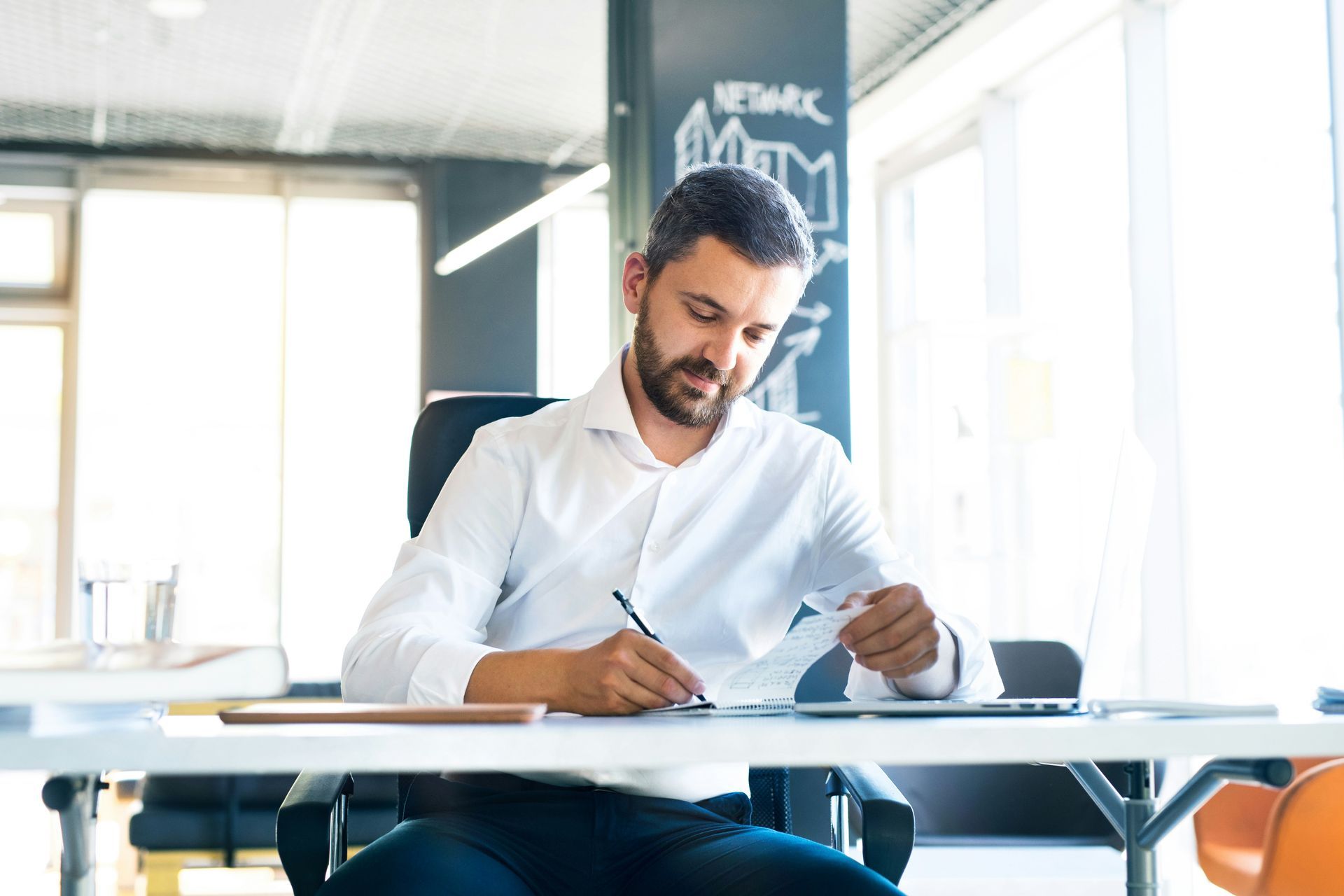 Man in a white shirt writing at a desk in a bright office