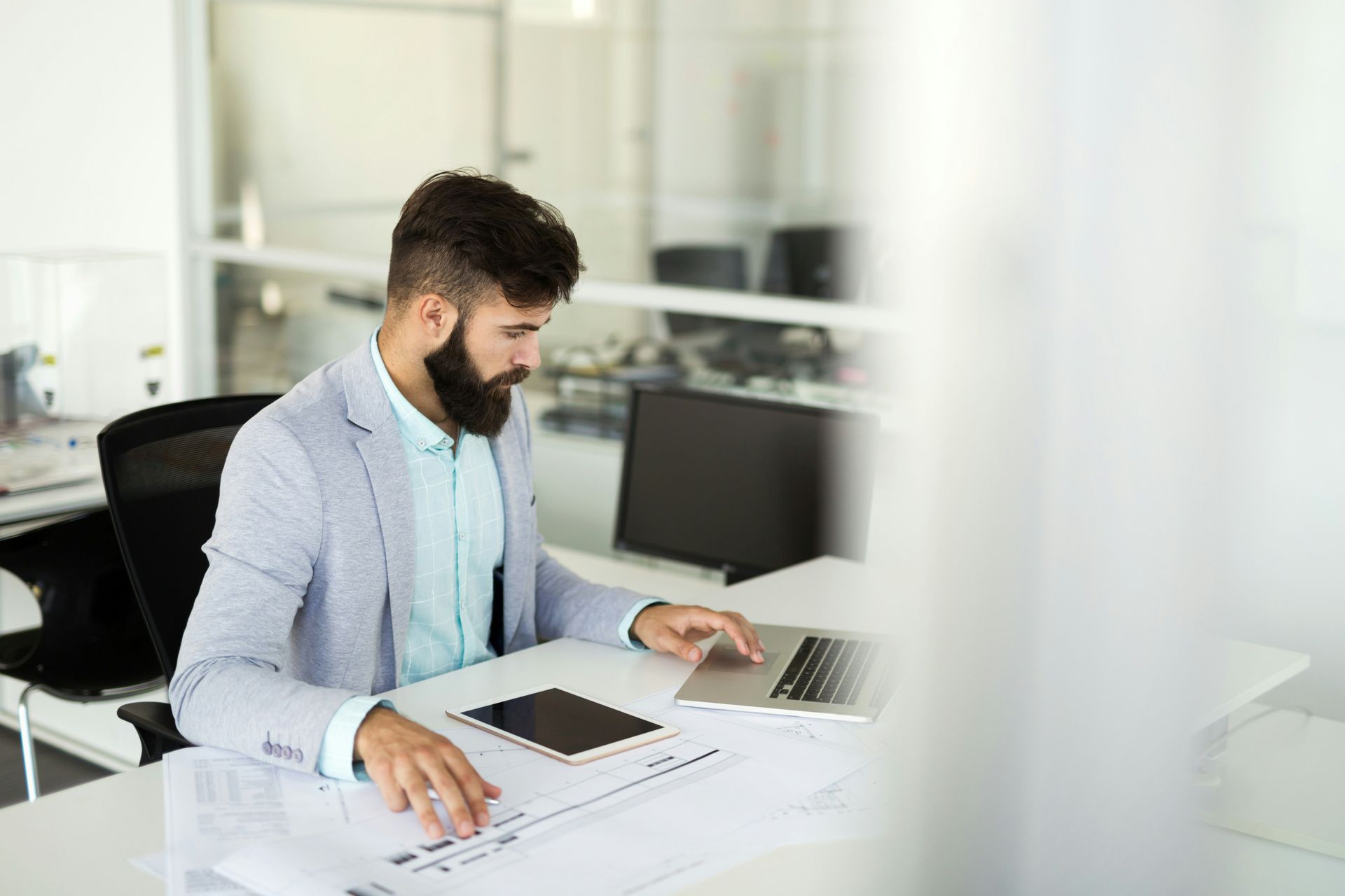 Man working at a desk with laptop and papers in a bright office