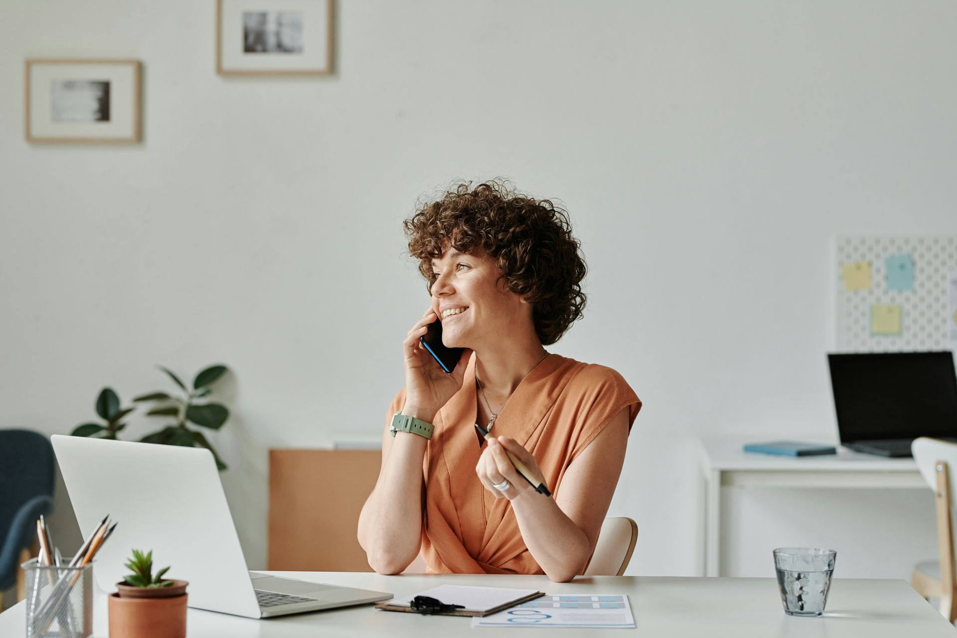 Person smiling and talking on the phone at a desk in a bright office