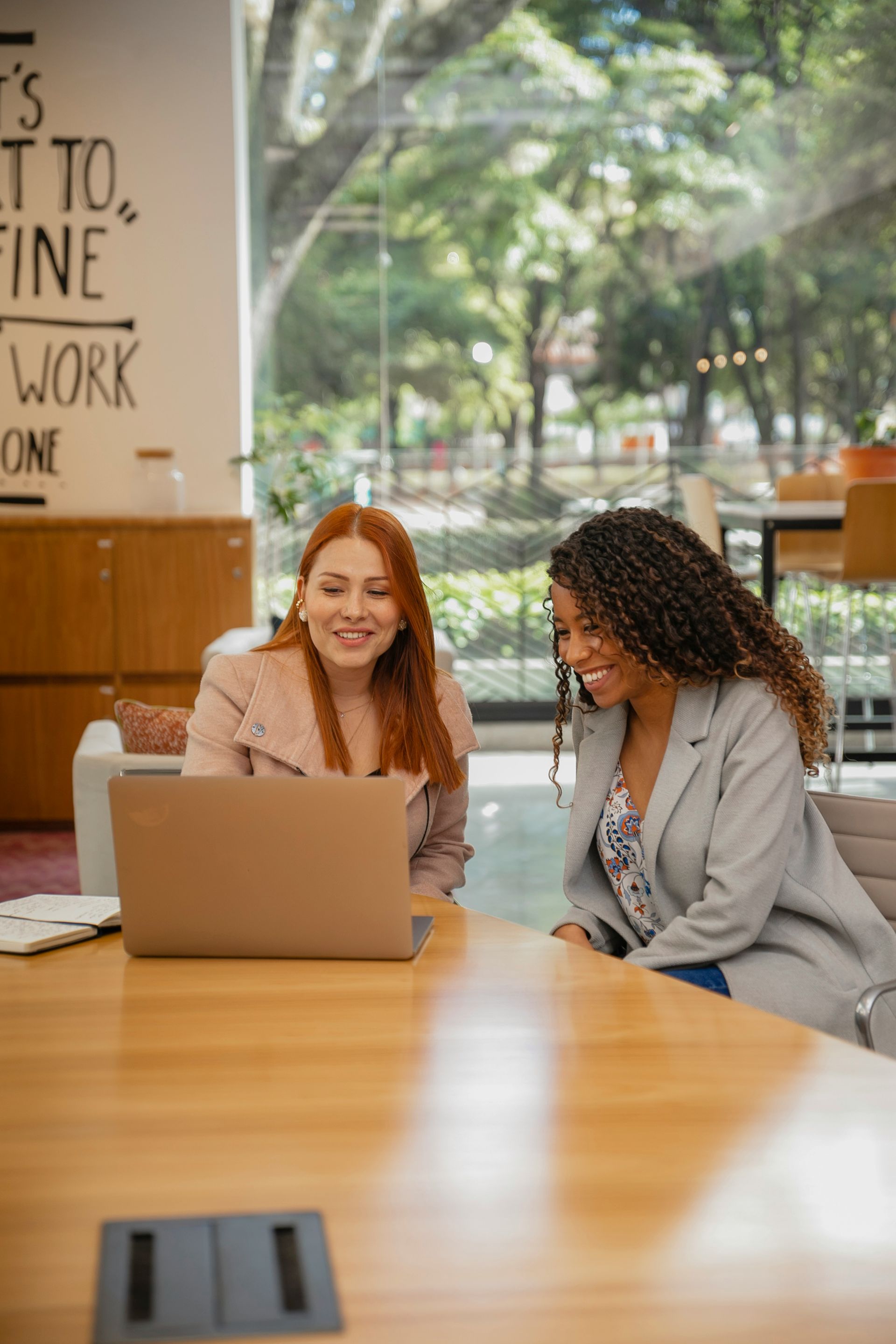 Two coworkers smiling at a laptop in a bright cafe with large windows