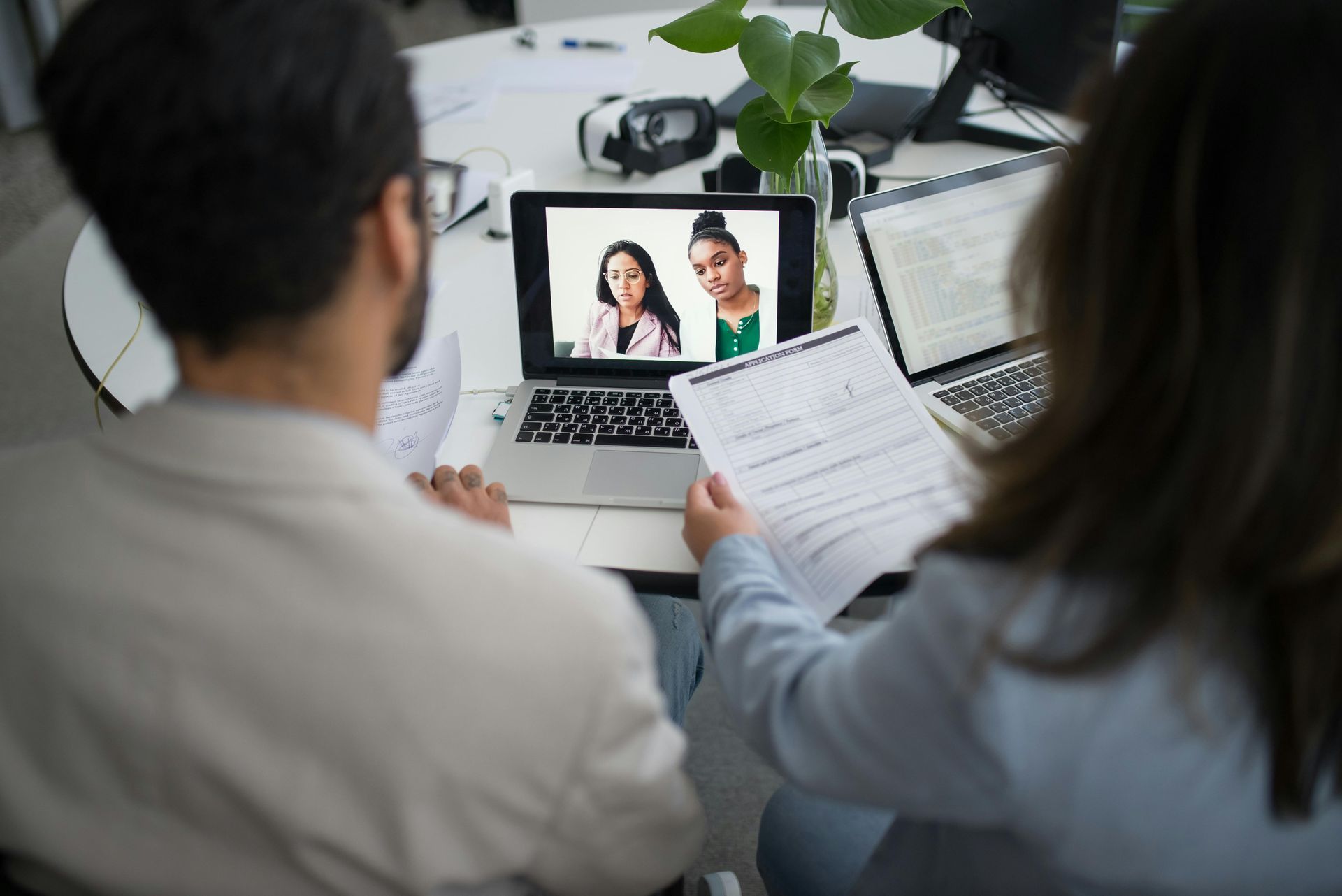 Two people in an office reviewing a laptop video call with documents in hand
