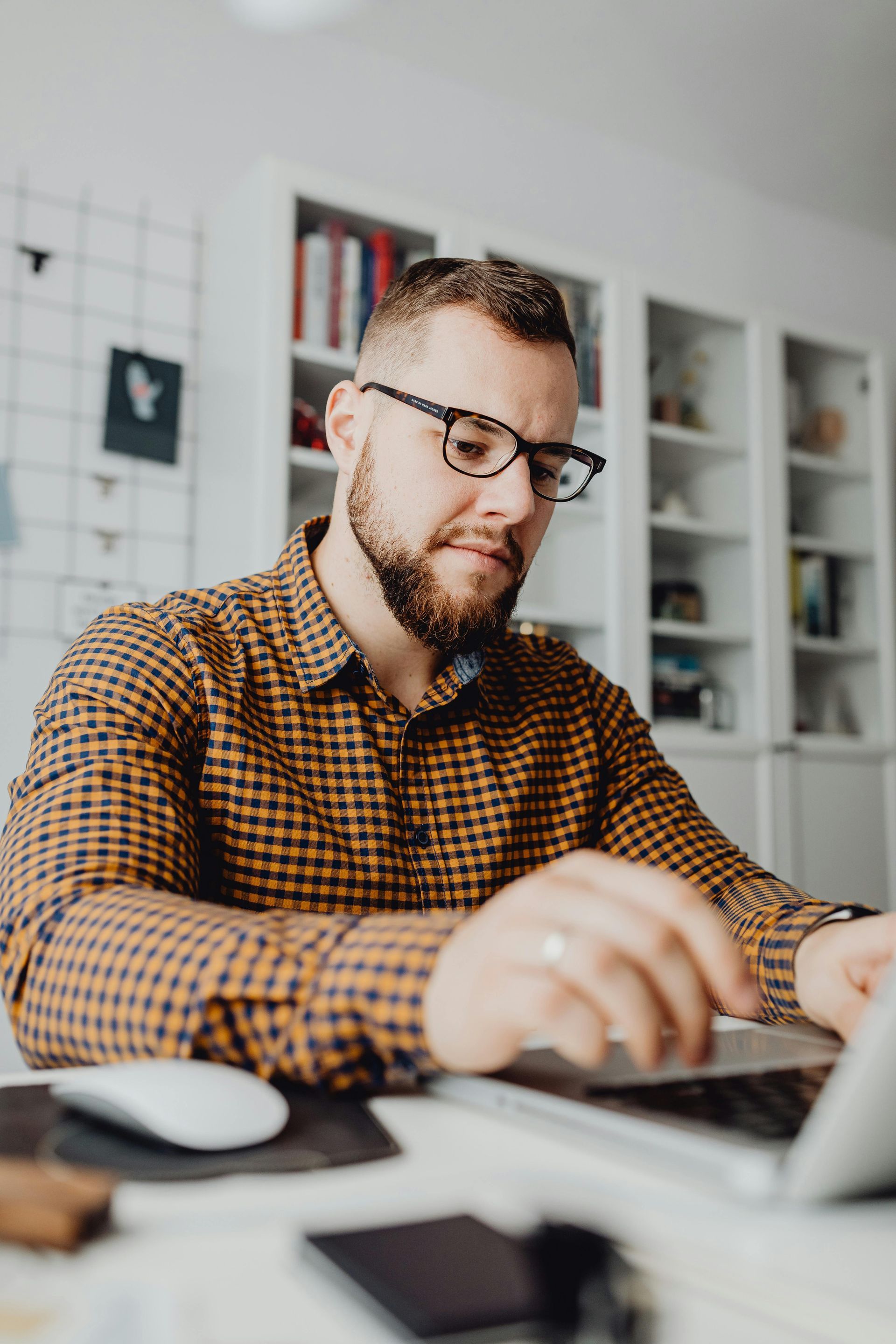 Man in glasses working on a laptop at a desk in a bright office