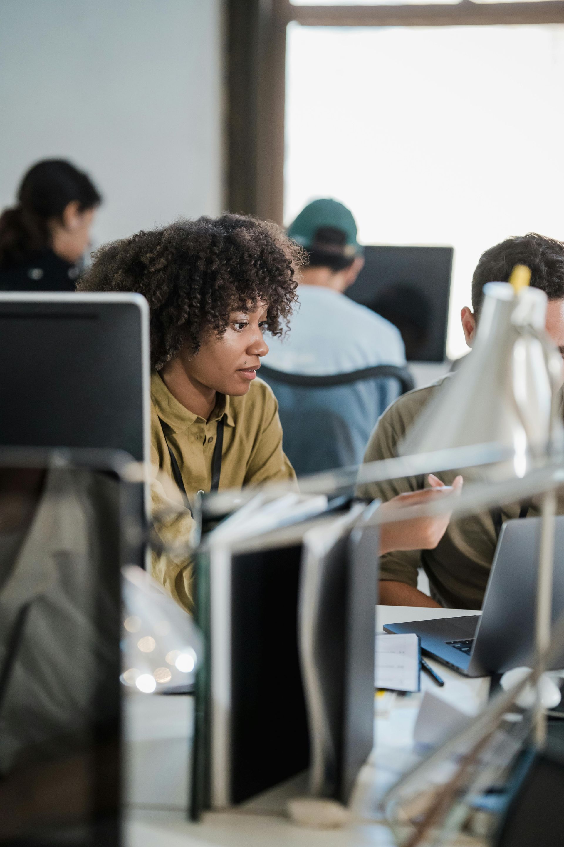 People working at desktop computers in an office, with one person focused in the foreground.