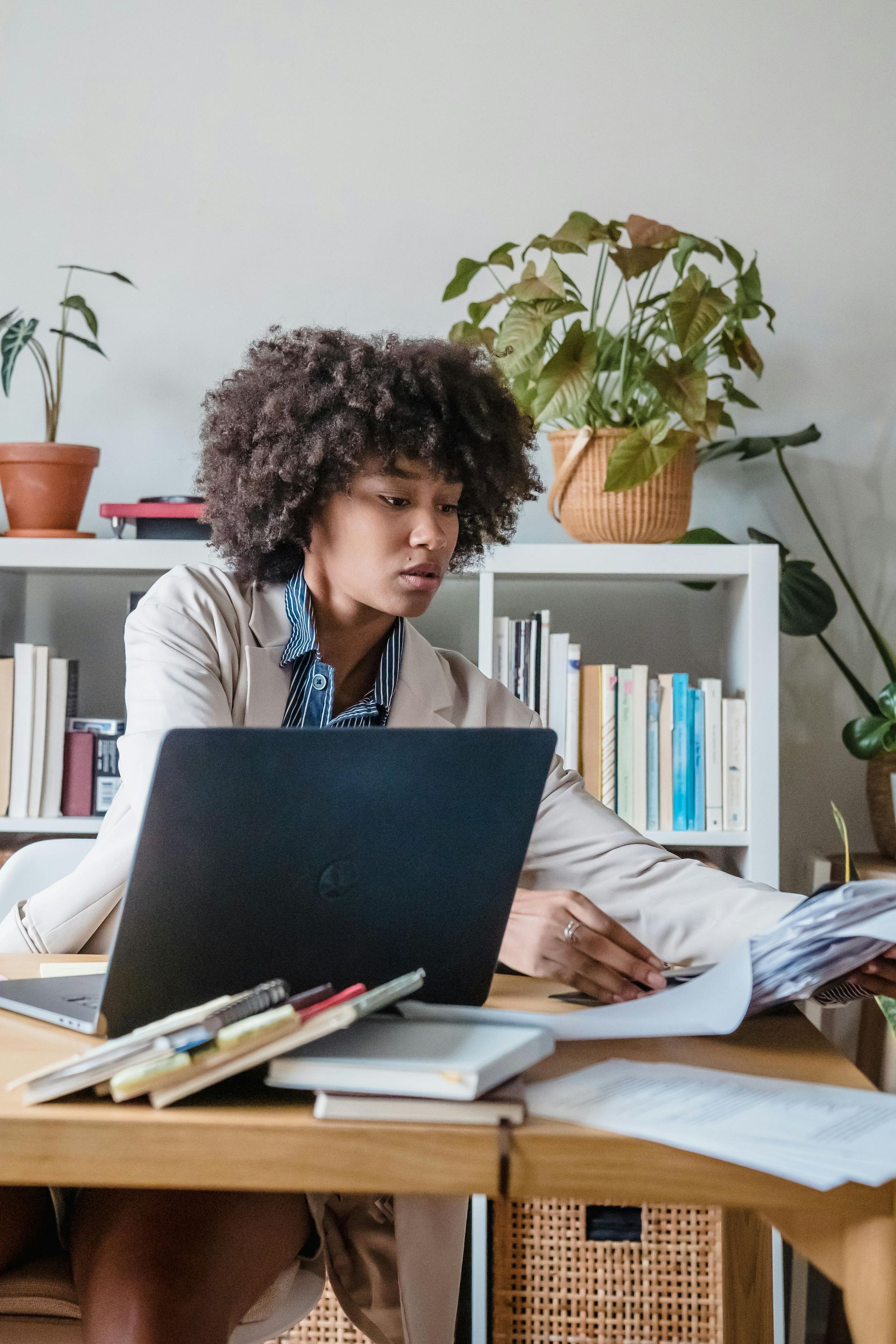 Person working at a desk with a laptop, papers, and plants in a home office