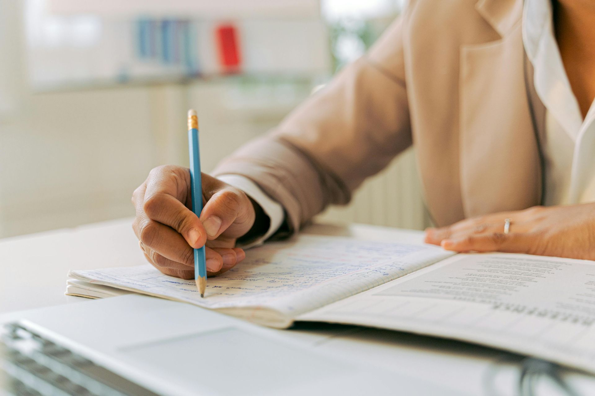 Hand writing with a pencil on an open notebook at a desk