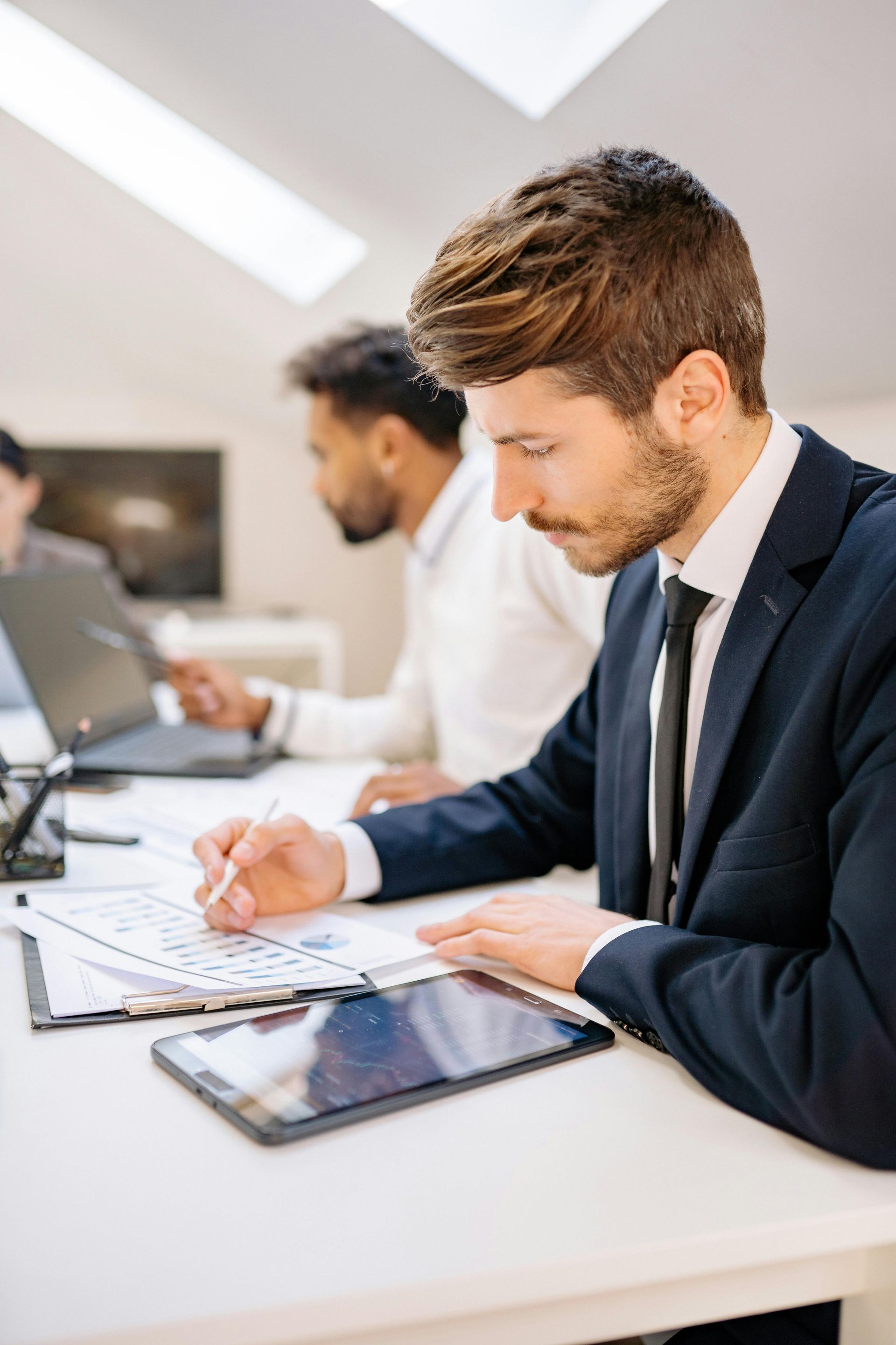 Business professional writing notes at a desk beside a tablet in a bright office