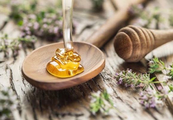 Honey dripping into a wooden spoon on a rustic table with wildflowers and a honey dipper with Amanda B Beauty and Brows.