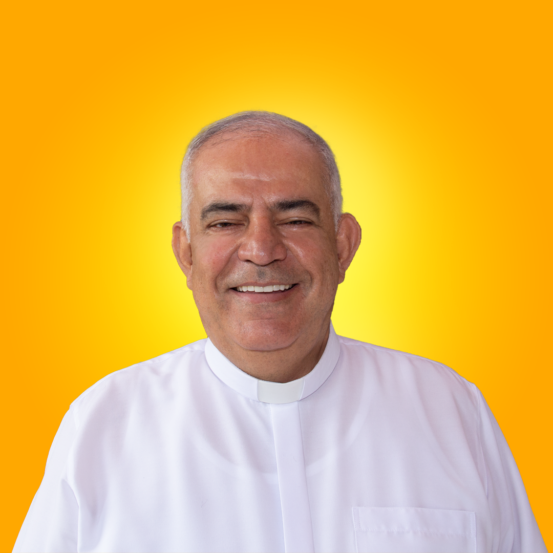 Miguel Alexis Saavedra Arias - Padre rector Un hombre con una camisa blanca sonríe delante de un fondo amarillo.