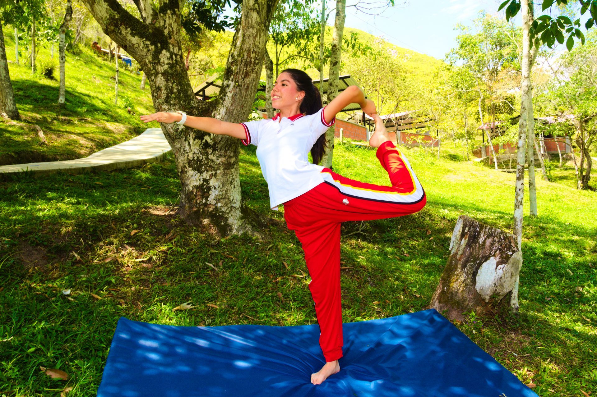 Una mujer está haciendo una pose de yoga sobre una colchoneta azul en un parque.
