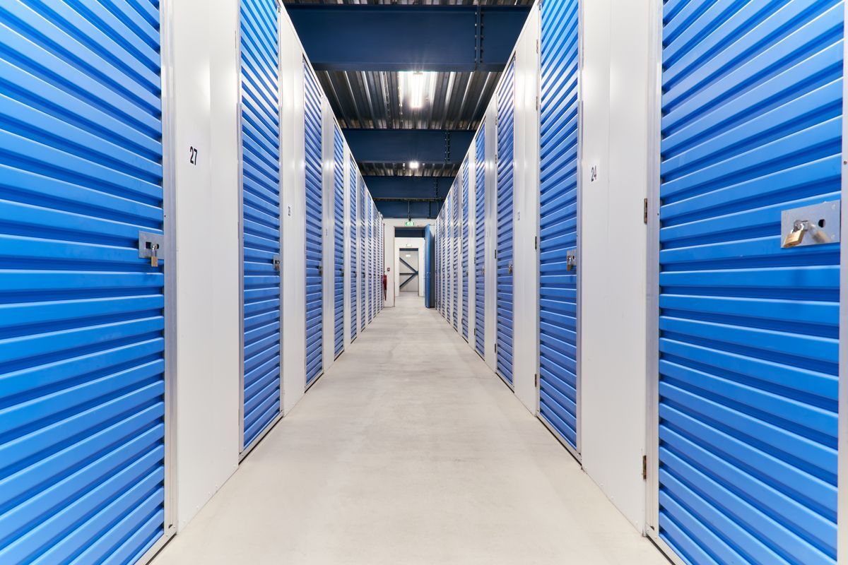 Long hallway of blue storage unit doors with white walls and concrete floor