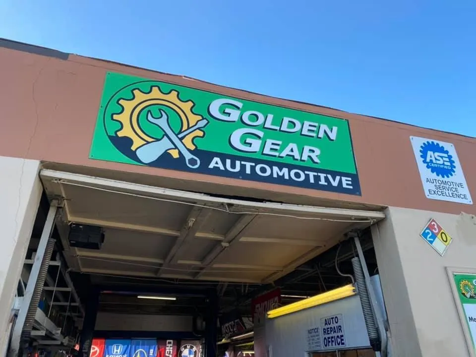 Golden Gear Automotive sign above open garage doors. Green and gold logo, blue sky. | Golden Gear Automotive