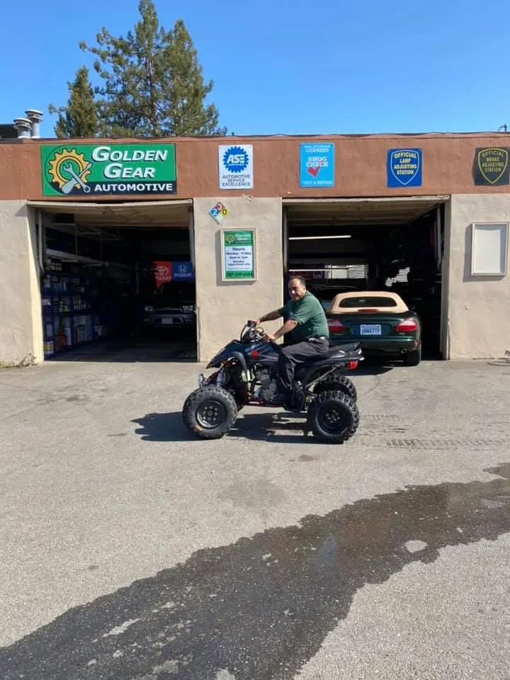 Man on an ATV in front of a Golden Gear Automotive shop. Sunny day, beige building, dark vehicle. | Golden Gear Automotive