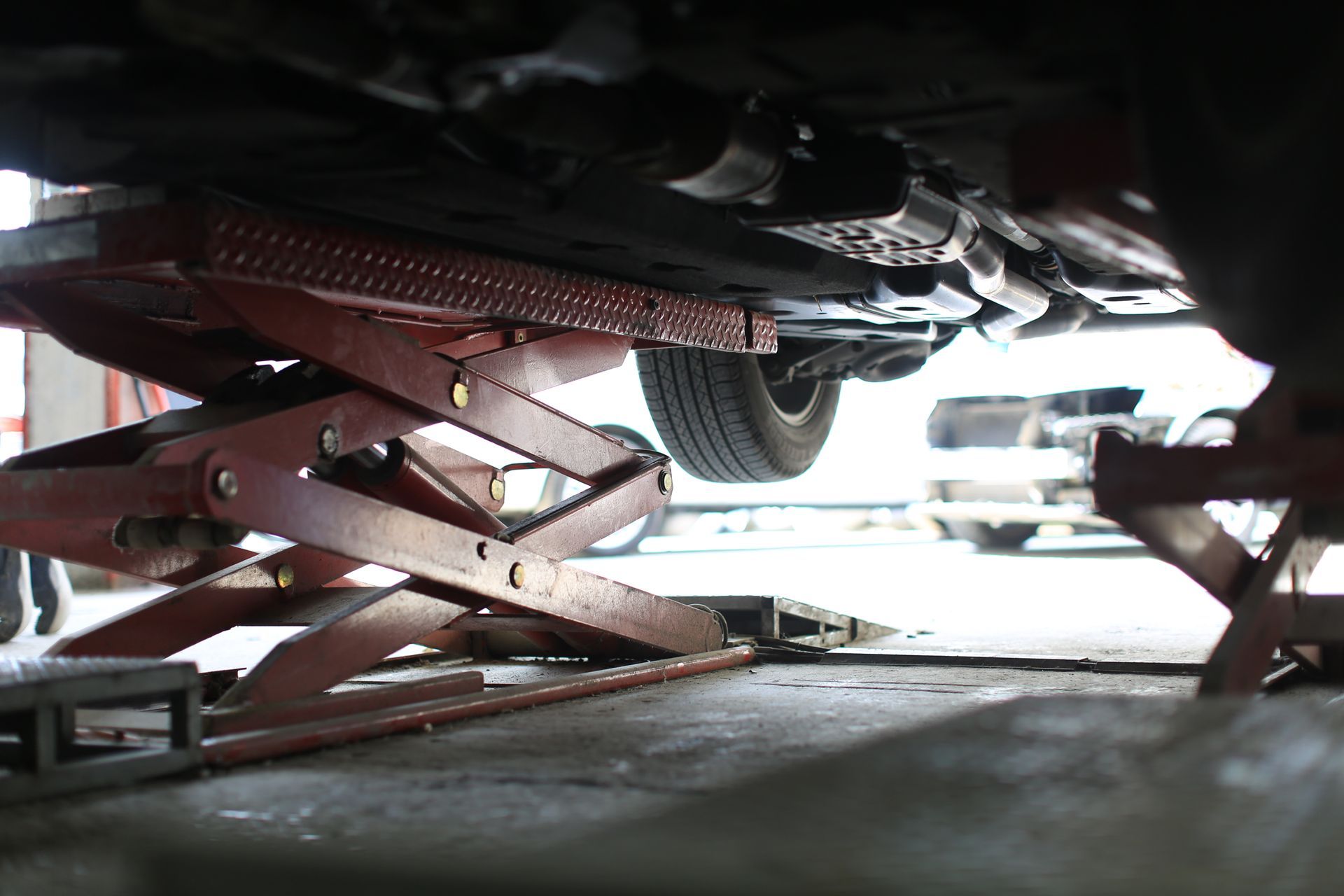 A car lifted on a red scissor lift inside a garage; tire visible, work underway. | Golden Gear Automotive