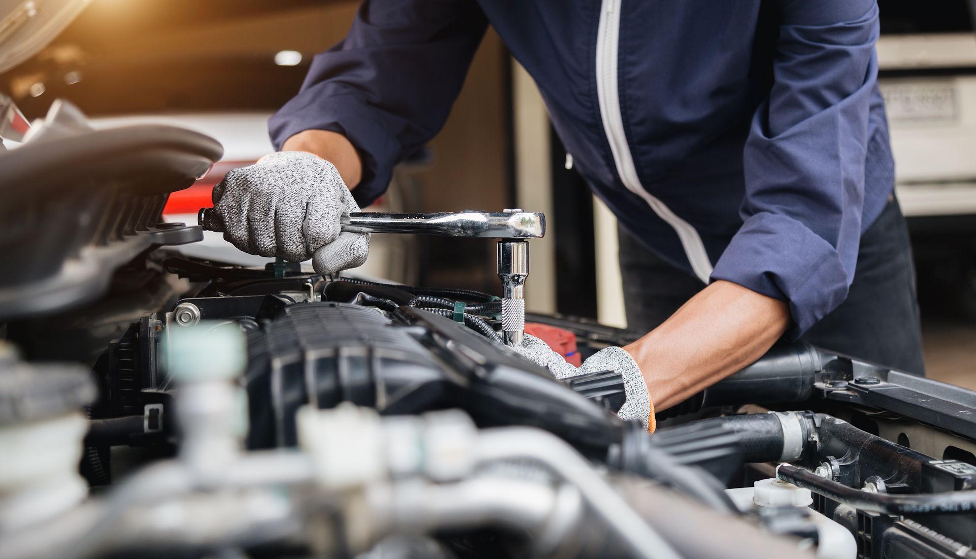 Mechanic in blue coveralls, using a wrench on a car engine. | Golden Gear Automotive