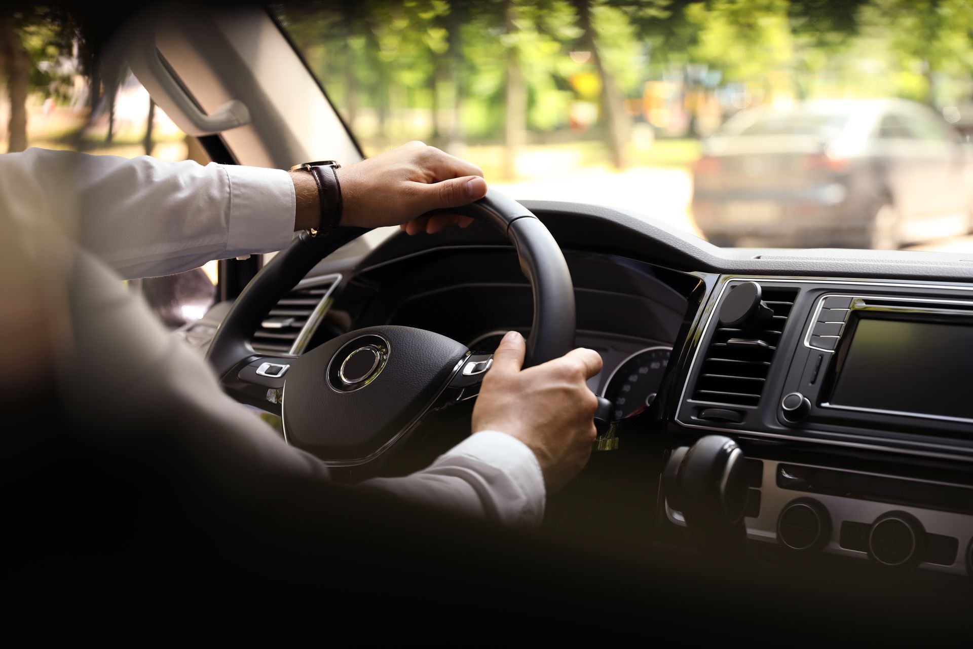 Hands gripping a steering wheel inside a car, driving on a sunny day. | Golden Gear Automotive