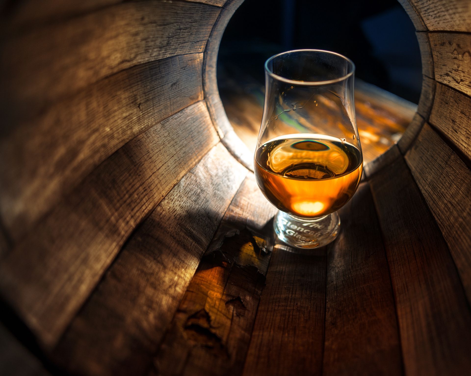 A glass of bourbon whiskey resting inside an oak aging barrel.