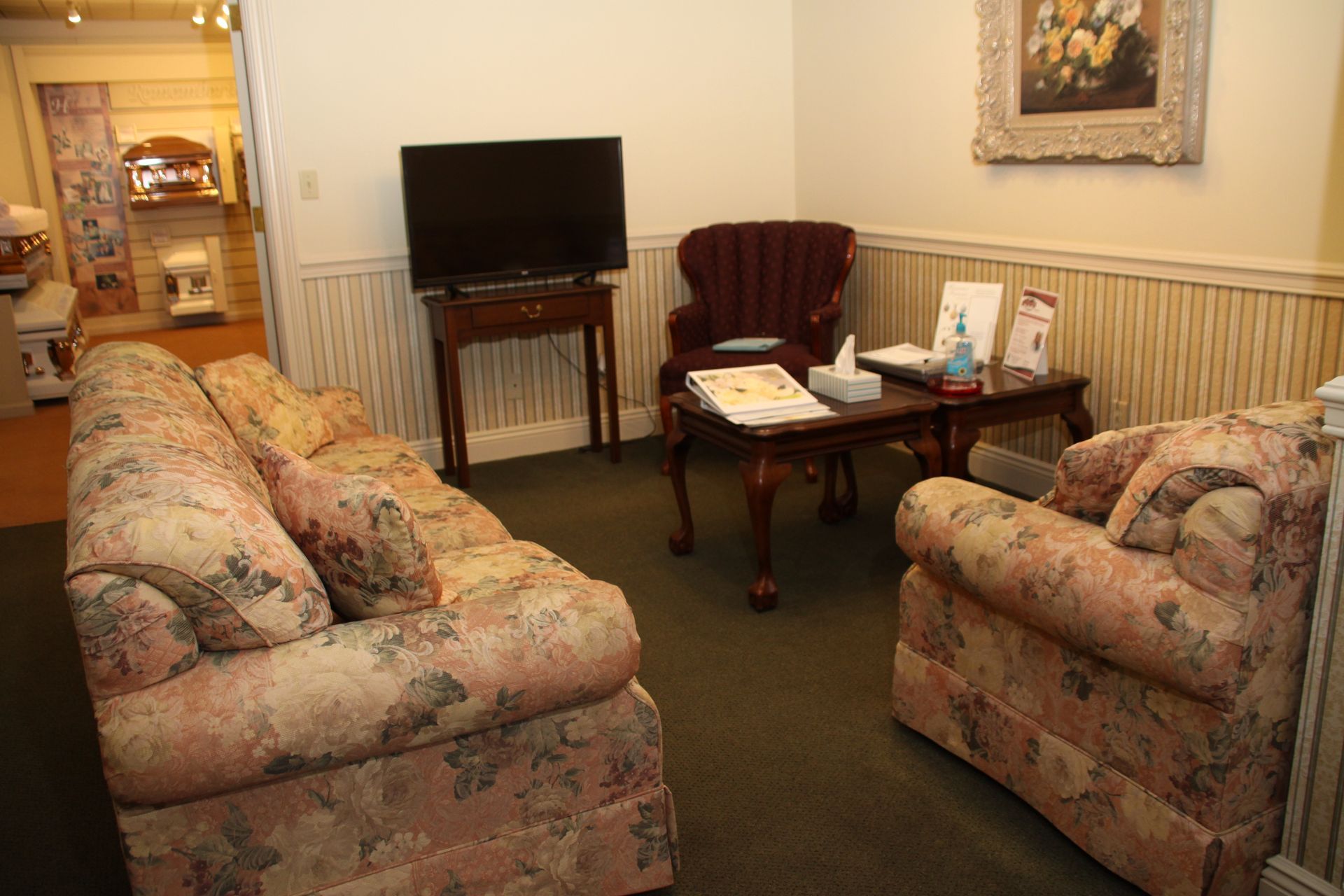 Small living room with floral sofas, TV, and side table near a doorway