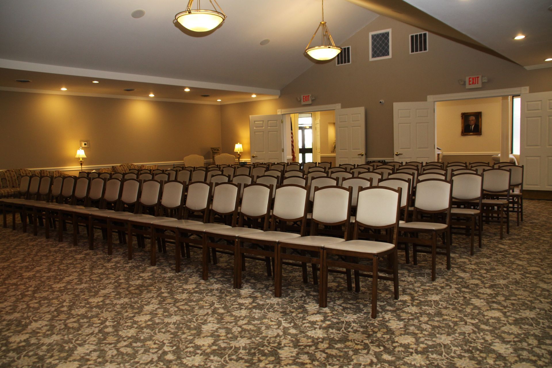 Empty banquet hall with rows of white chairs facing the front under warm ceiling lights