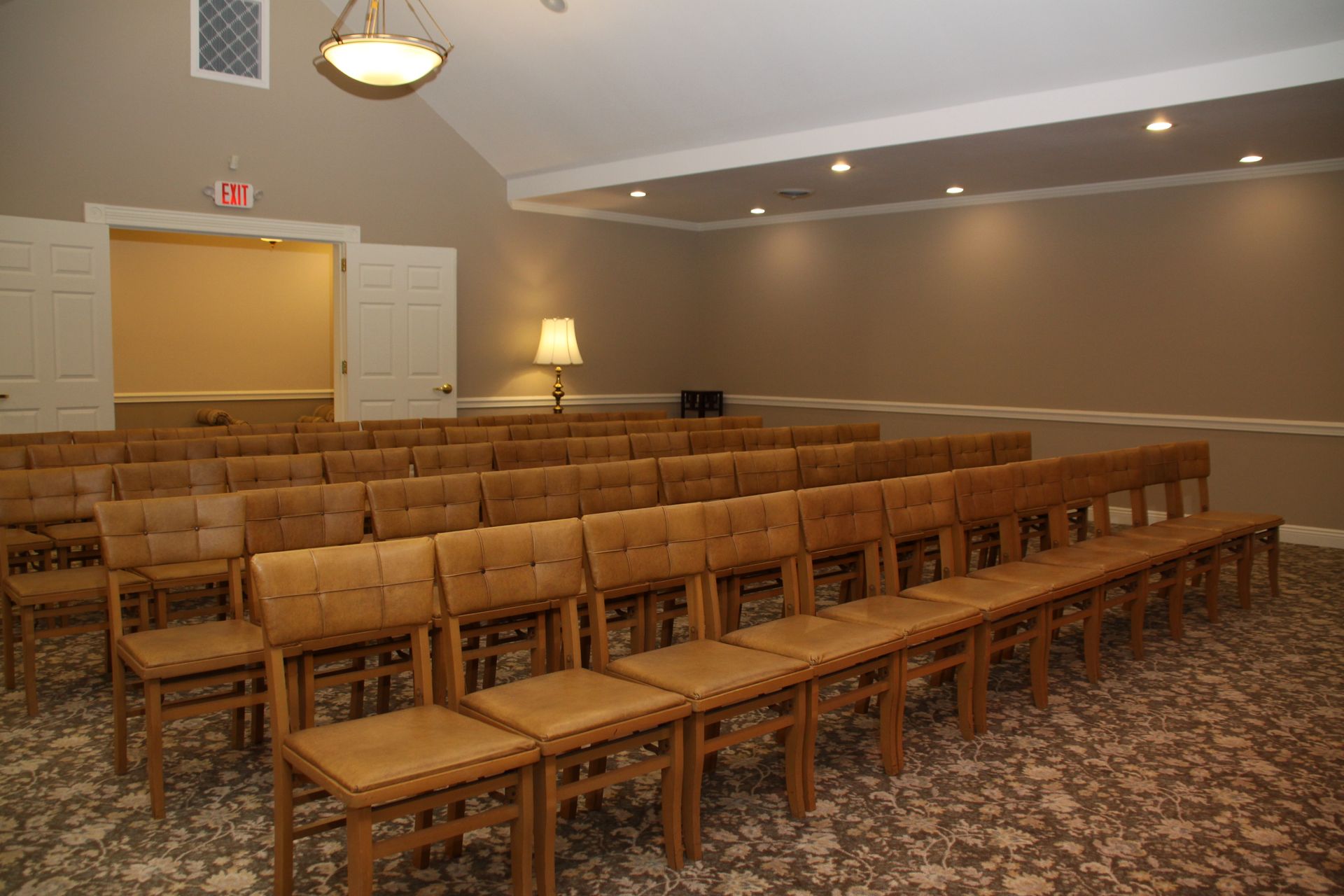 Empty conference room with rows of wooden chairs, beige walls, and a patterned carpet.