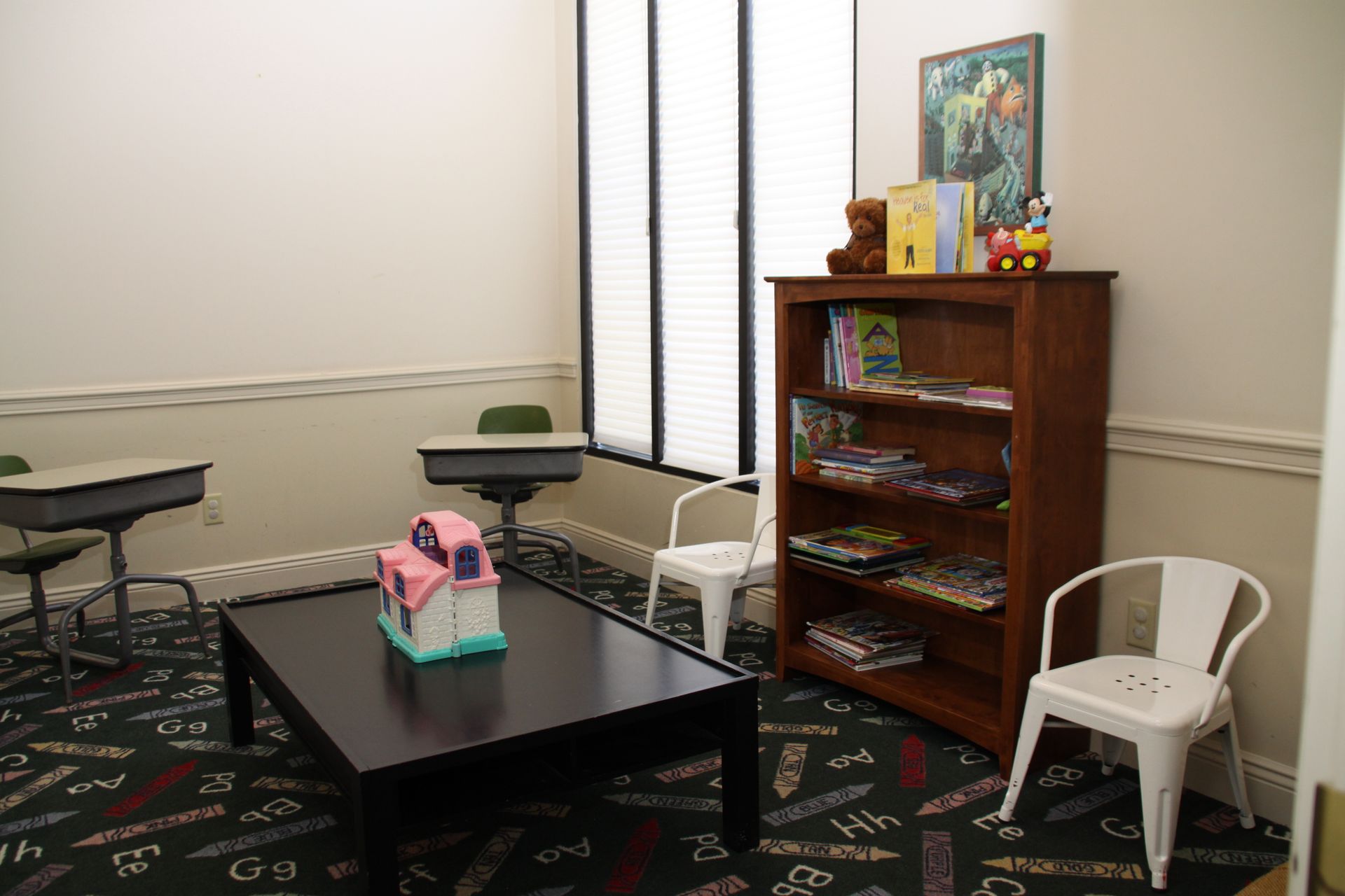 Classroom corner with tables, chairs, a bookshelf, and a small black table with a pink bag on top